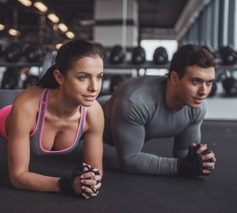 Attractive young muscular man and woman doing plank exercise while working out in gym